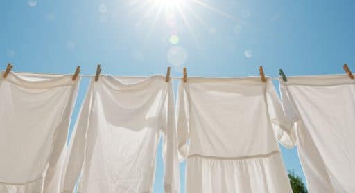 Imagem de roupas brancas dependuradas no varal com o céu azul ao fundo