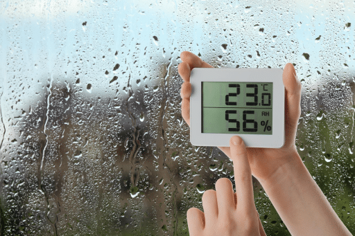 imagem de uma janela umida, é possível ver um termostato com a temperatura do ambiente e do porcentagem de umidade no ar.