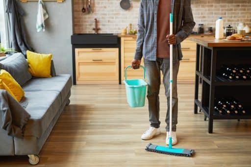 O ChatGPT disse: Pessoa limpando o chão de uma cozinha moderna com esfregão e balde, em ambiente bem decorado com sofá e almofadas amarelas.