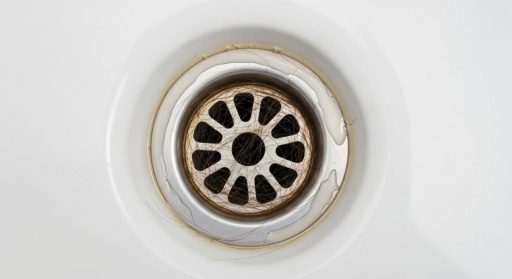 Ralo de pia ou box com acúmulo de fios de cabelo, indicando necessidade de limpeza.